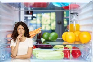 un frigo pieno di alimenti ed una persona dubbiosa