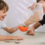 bambino sorrideva mentre gli viene riempita la tazza di cereali