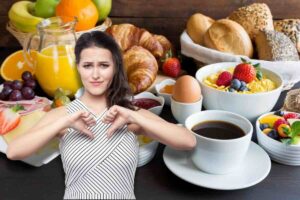 Donna pollici in giù, dietro di lei tavolo imbandito per colazione con caffè, cornetti, porridge, cereali, uovo, spremuta