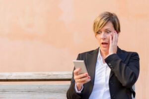 donna con il cellulare in mano e l'espressione sconvolta che si tocca il viso con una mano