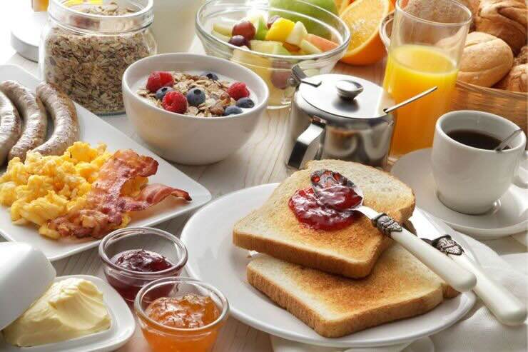 Tavolo imbandito con fette biscottate e marmellate, porridge, frutta