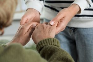una donna anziana che stringe le mani ad una persona più giovane che la sostiene