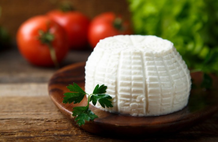 ricotta sopra ad un tagliere e dietro dei pomodori