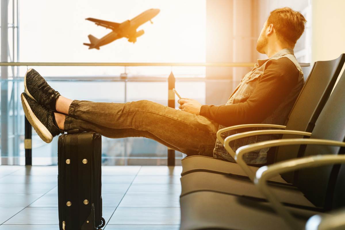 uomo all'aeroporto con la valigia seduto che aspetta il suo volo