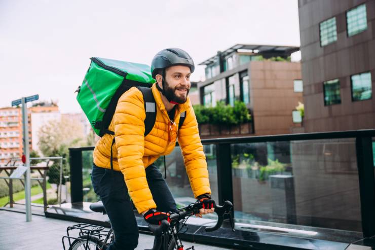 Un rider in bicicletta con lo zaino contenitore sulle spalle che lavora