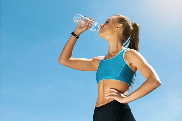 Ragazza beve da bottiglia d'acqua mentre è vestita per fare sport