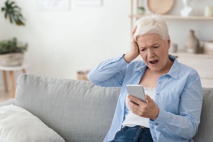 Anziana donna sul divano guarda il cellulare incredula