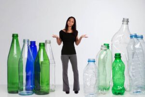 Sulla sinistra delle bottiglie in vetro e sulla destra delle bottiglie in plastica ed al centro un ragazza indecisa