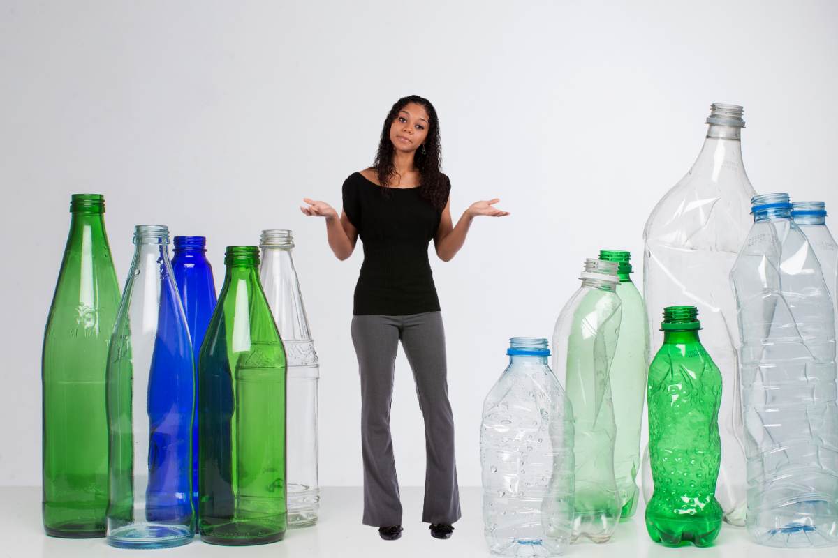 Sulla sinistra delle bottiglie in vetro e sulla destra delle bottiglie in plastica ed al centro un ragazza indecisa